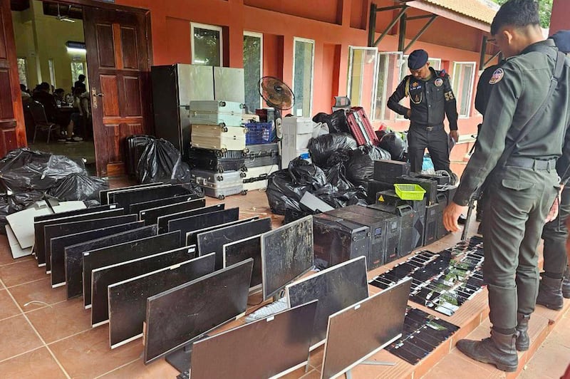 This July 17, 2025, image distributed by Cambodian national news agency Agence Kampuchea Presse (AKP) shows military police looking at computers, smartphones and other equipment seized during a raid on a scam center in Kandal province.