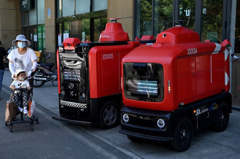 People walk past Chinese e-commerce giant JD.com's autonomous vehicles used to deliver goods to customers, outside a supermarket in Beijing, June 18, 2021. Credit: AFP